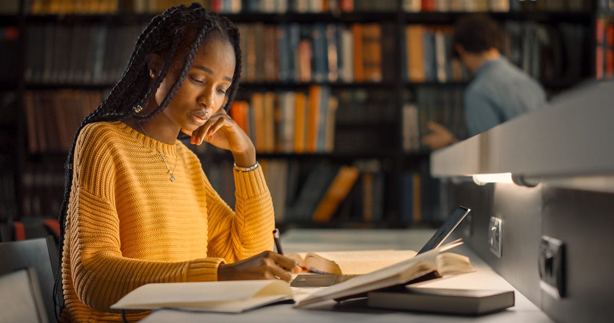 University Library: Gifted Black Girl uses Laptop, Writes Notes - Foto: Gorodenkoff (Adobe Stock: 356426676)